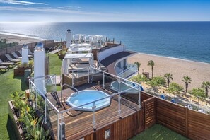 A deck with a hot tub, lounge chairs, and a view of the beach. - Hotel GHT Marítim (Calella)