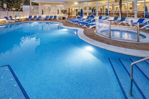 Una piscina techada, una piscina al aire libre, sombrillas