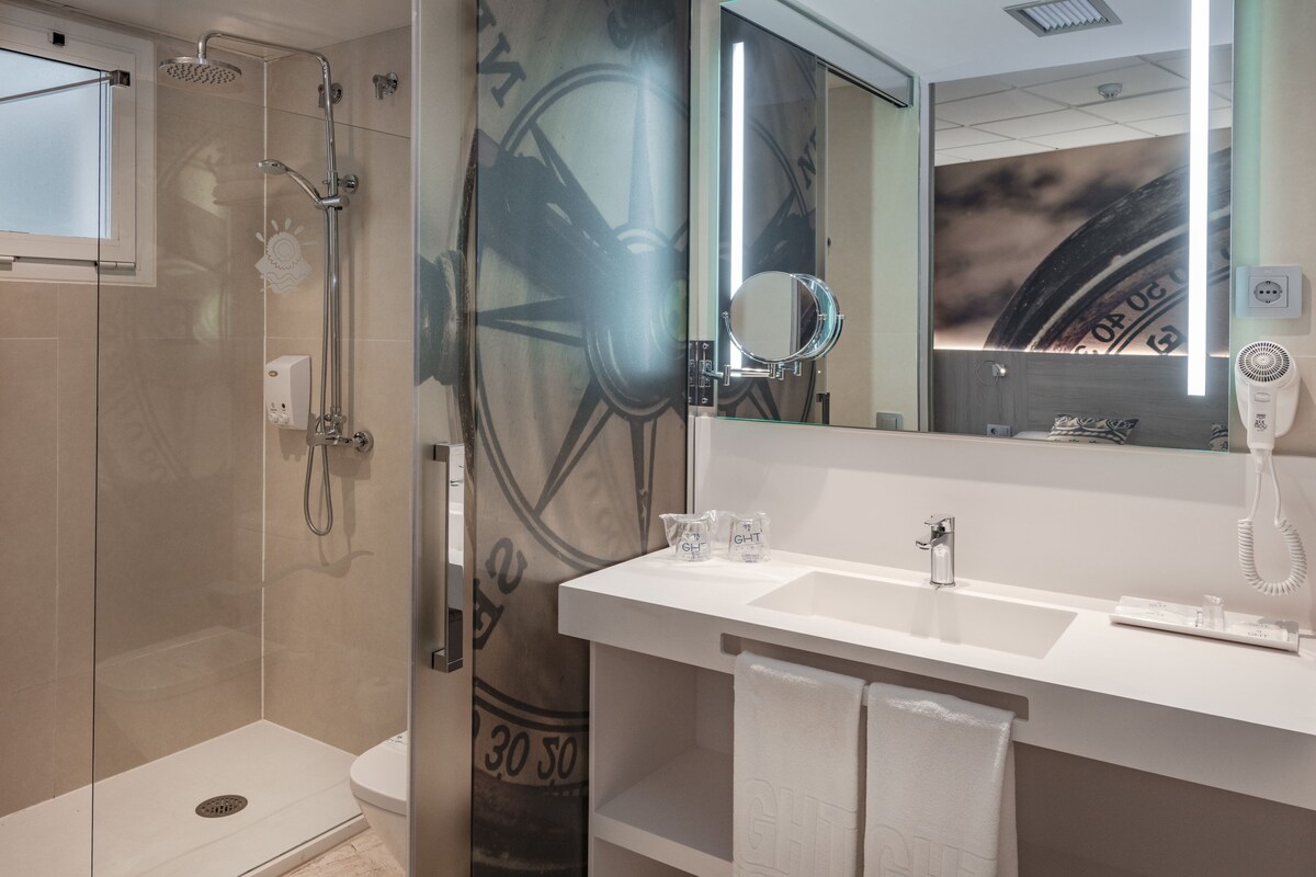 A modern bathroom with a glass-enclosed shower, a large mirror, a white sink, and a towel rack.