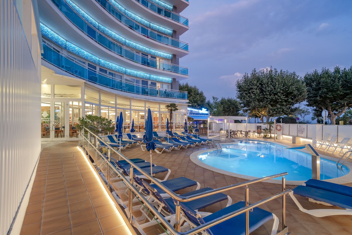 A cruise ship deck with a swimming pool, sun loungers, and a restaurant area.