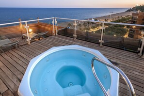 A wooden deck with a hot tub, lounge chairs, and a view of the beach and ocean.