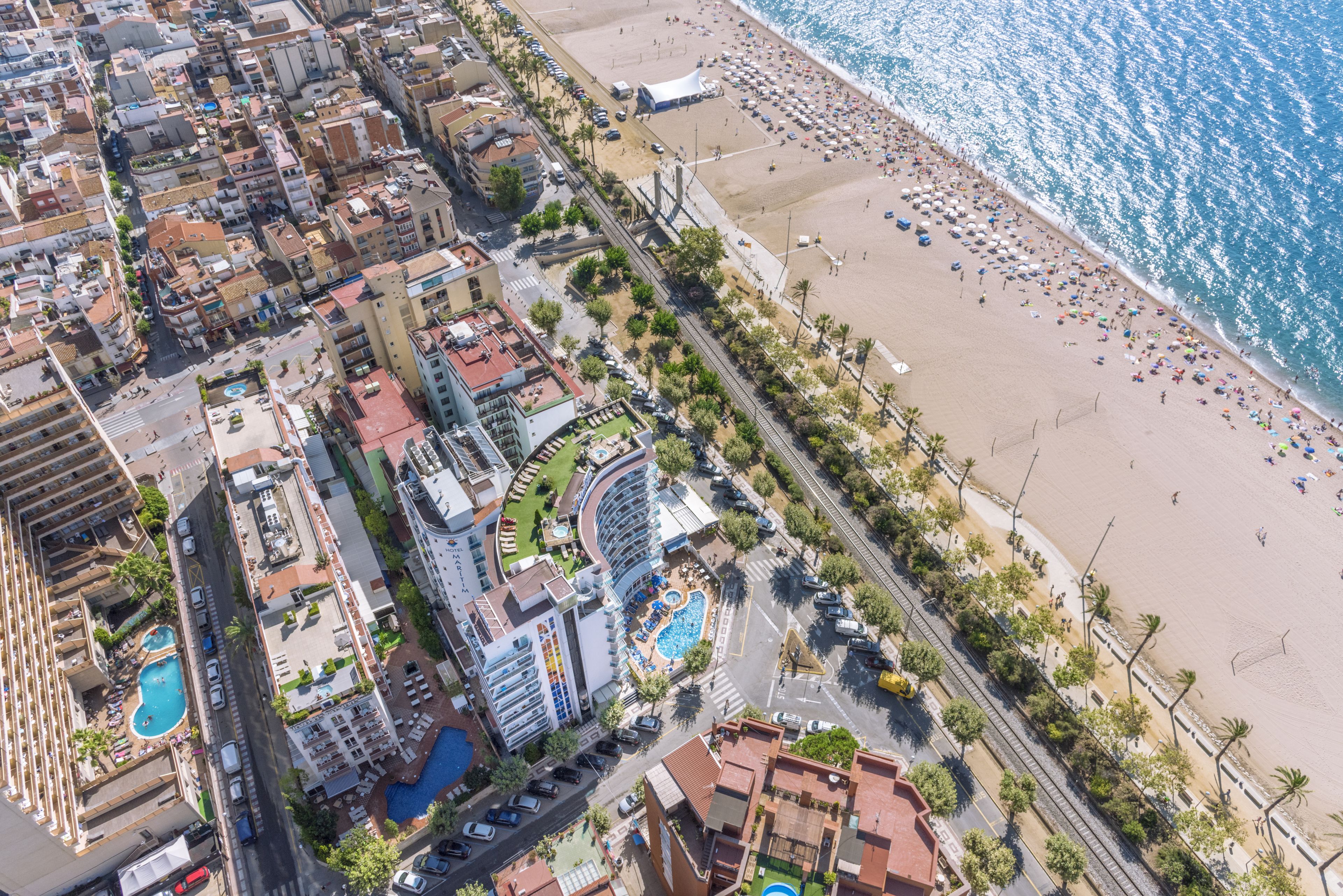 Vista aérea de una ciudad costera con una playa, un hotel con piscina y edificios urbanos densos.