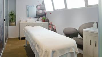 A clean, modern spa room with a massage table, a small plant, a towel rack, and a sink.
