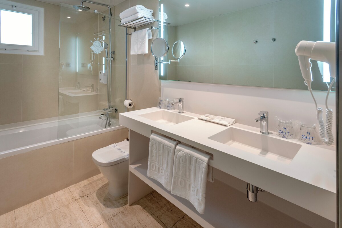 A modern bathroom with a glass-enclosed shower, a white sink with two mirrors, and a hairdryer on the counter.