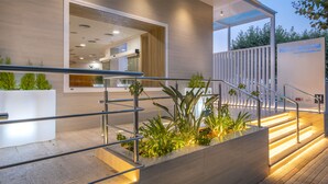 Una entrada de hotel moderna con escaleras, barandas de metal y plantas en macetas.