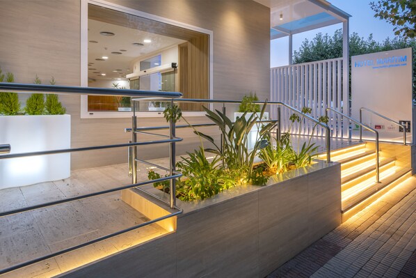 Una entrada de hotel moderna con escaleras, barandas de metal y plantas en macetas.