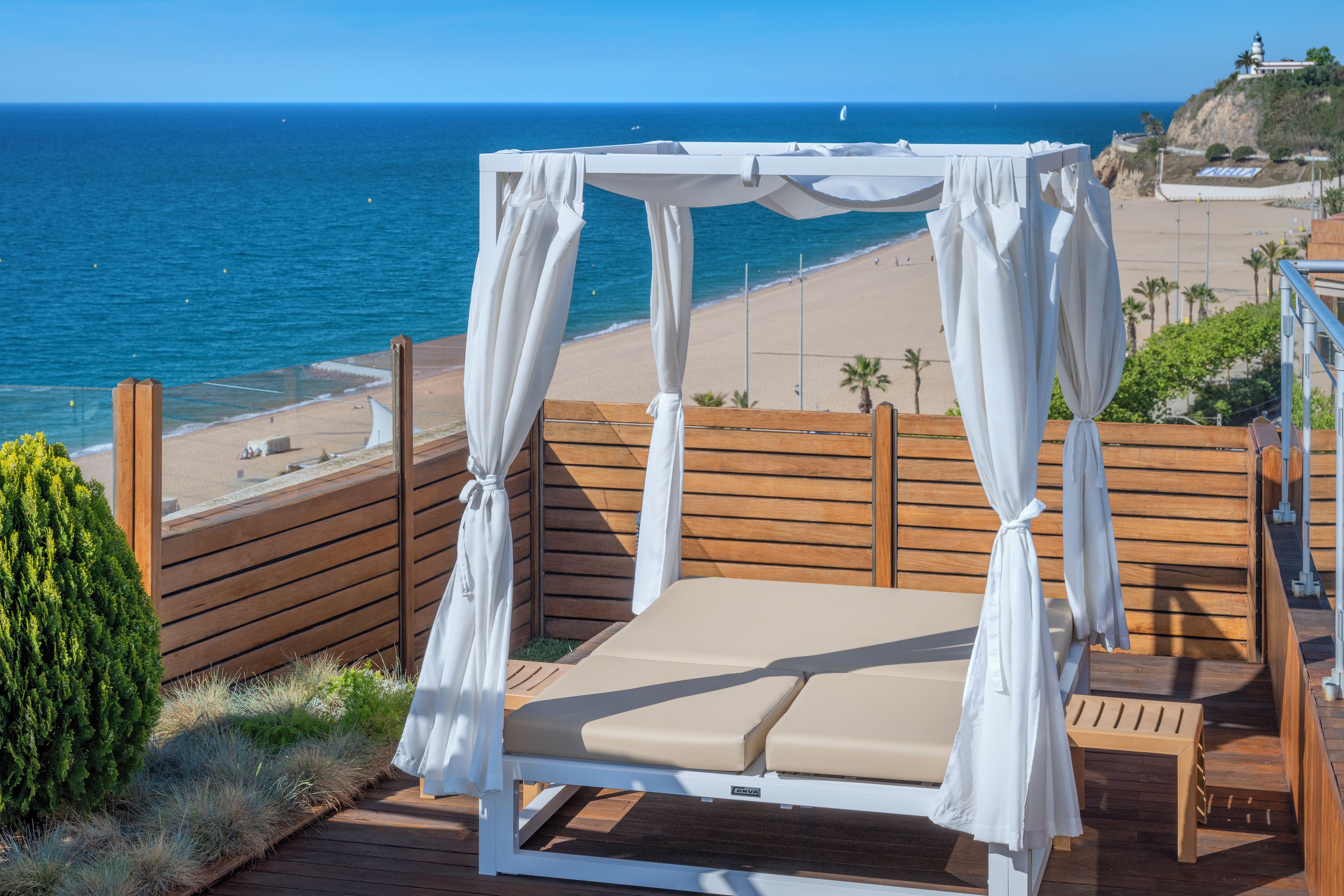 A beachside balcony with a canopy bed, wooden deck, and a view of the ocean.
