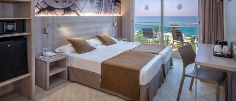 A hotel room with a bed, bedside tables, a desk, and a view of the ocean.