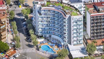 A hotel with a curved glass facade, a rooftop pool, and multiple balconies.