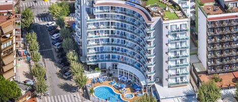 A hotel with a curved glass facade, a rooftop pool, and multiple balconies.