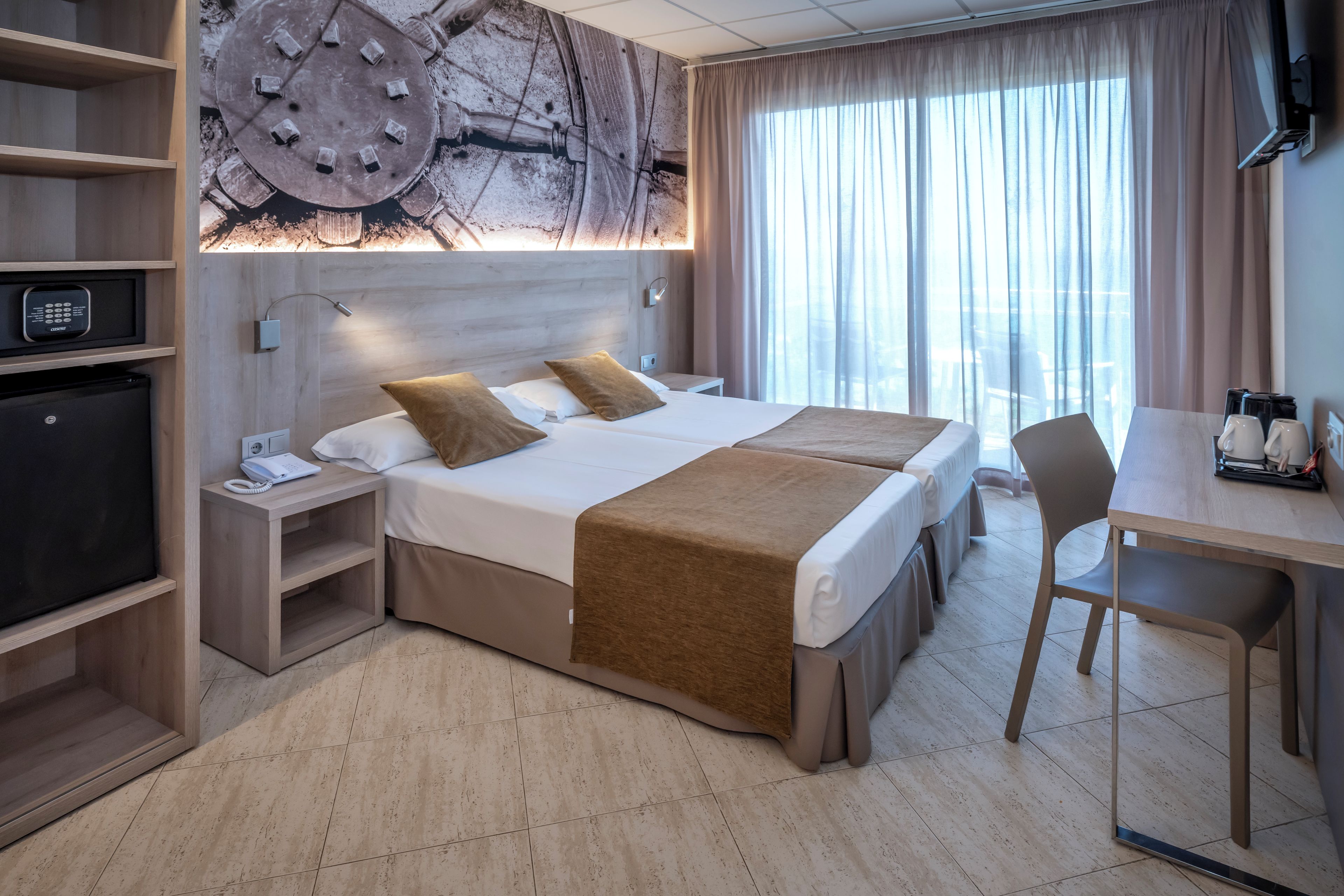 Een hotelkamer met een bed, nachtkastjes, een bureau, een stoel, een televisie en een groot raam met gordijnen.