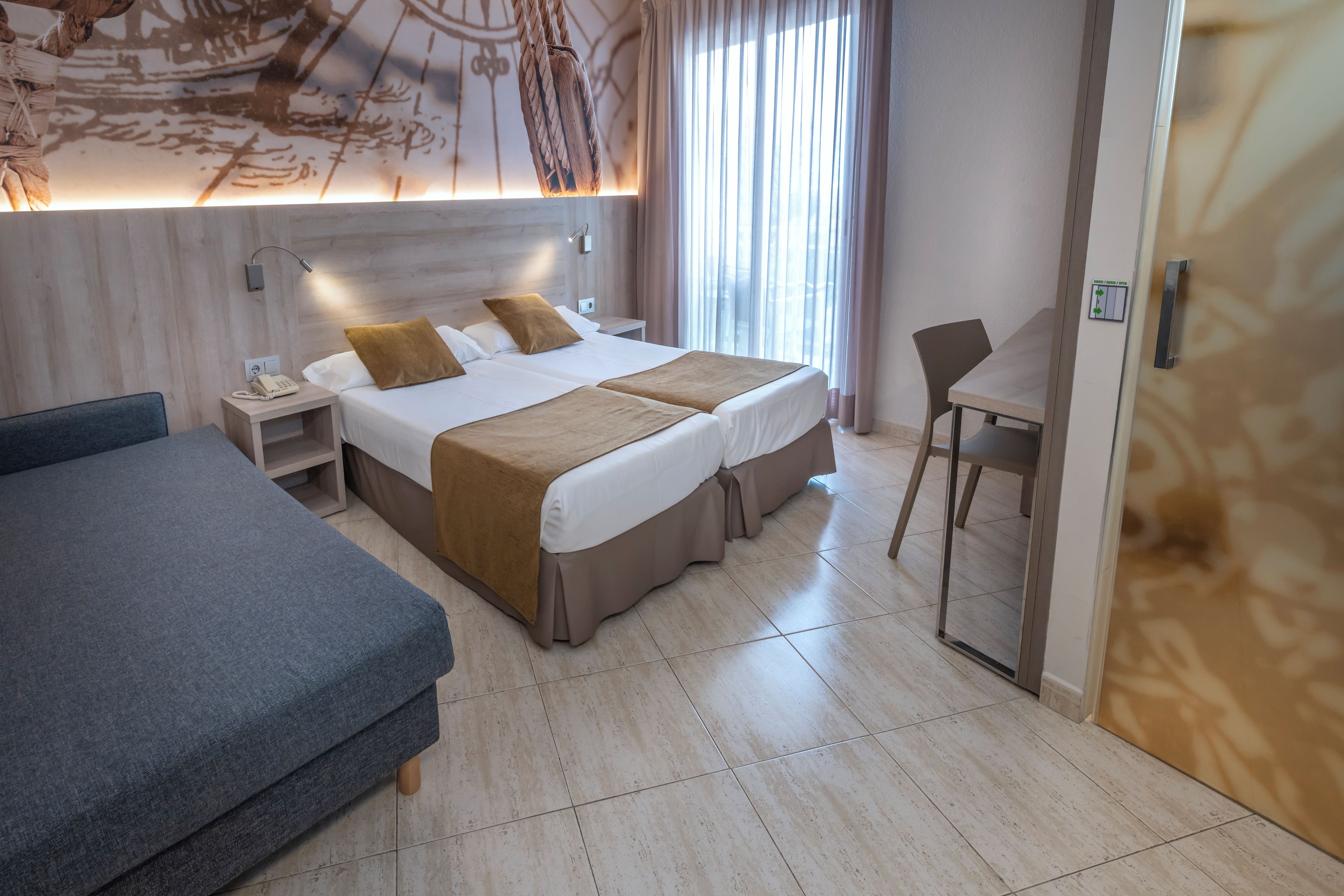 Una habitación de hotel con una cama grande, una cama más pequeña, un escritorio y una silla.