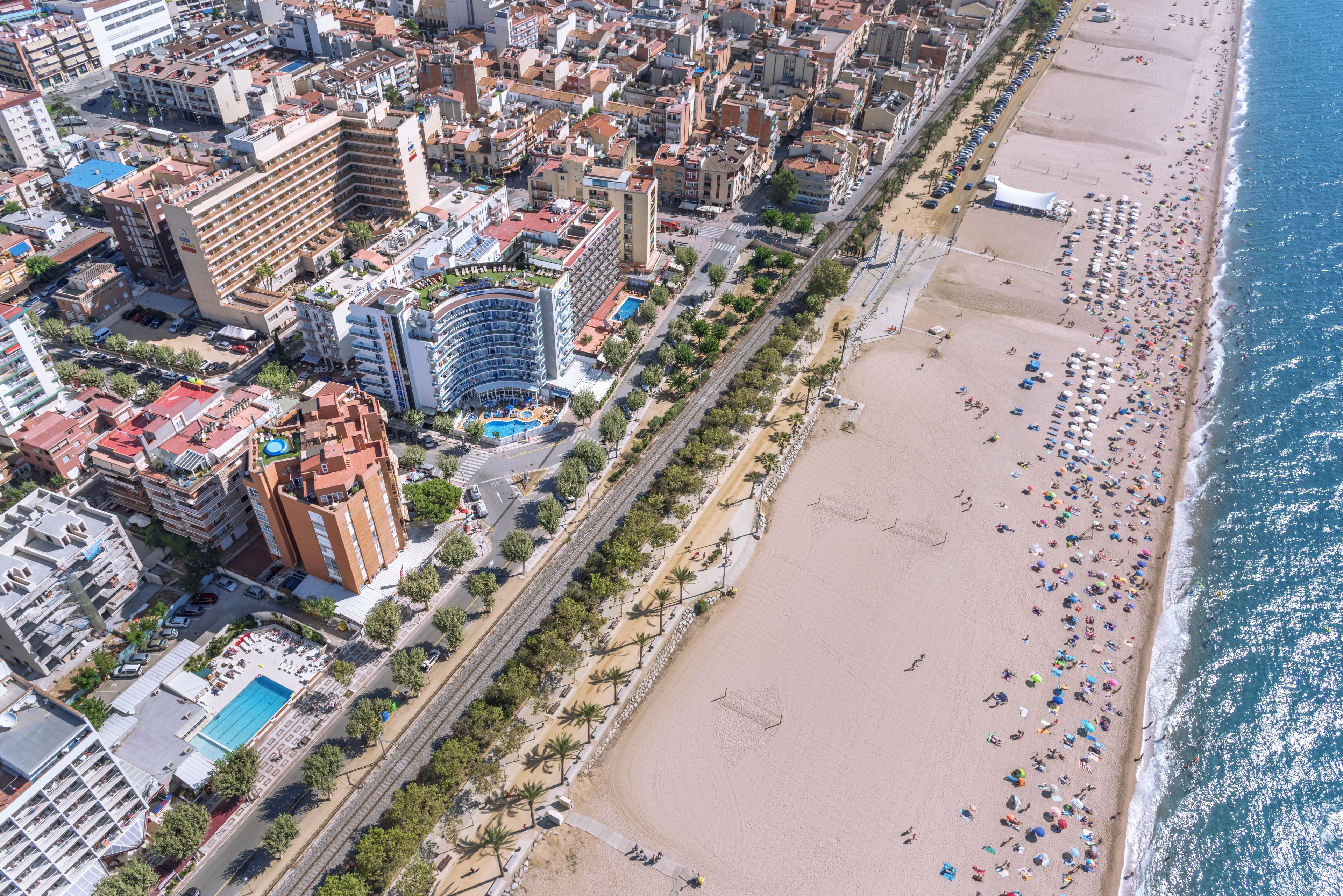 An aerial view of a coastal city with a beach, hotels, and a road running parallel to the shore.