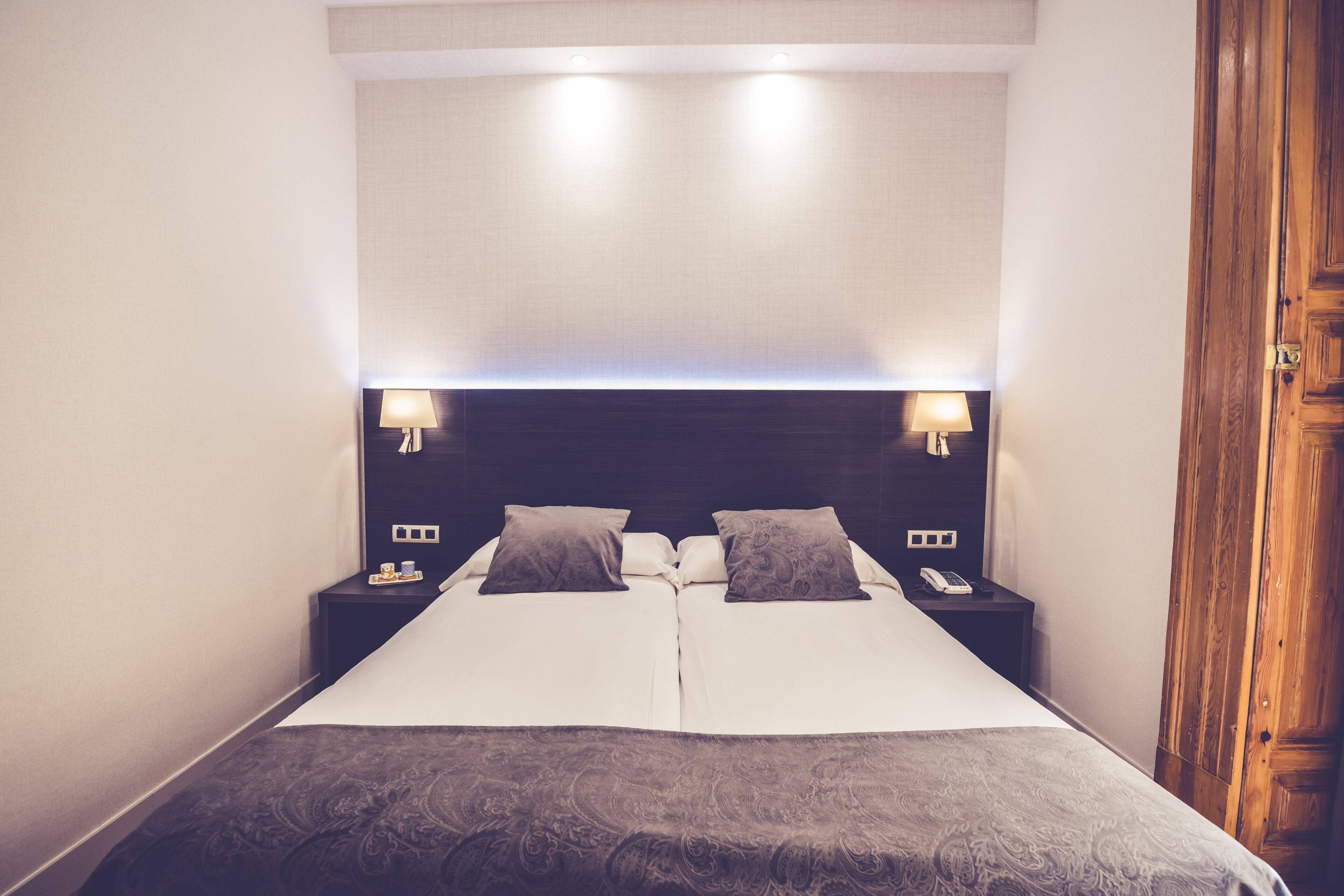 A double bed with a dark patterned bedspread, two bedside tables with lamps, and a wooden wardrobe.