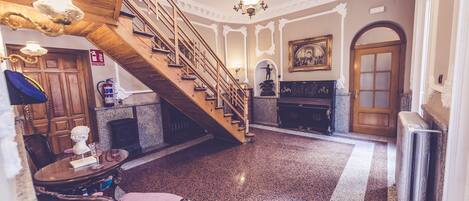A grand lobby with a wooden staircase, a fireplace, and a chandelier.