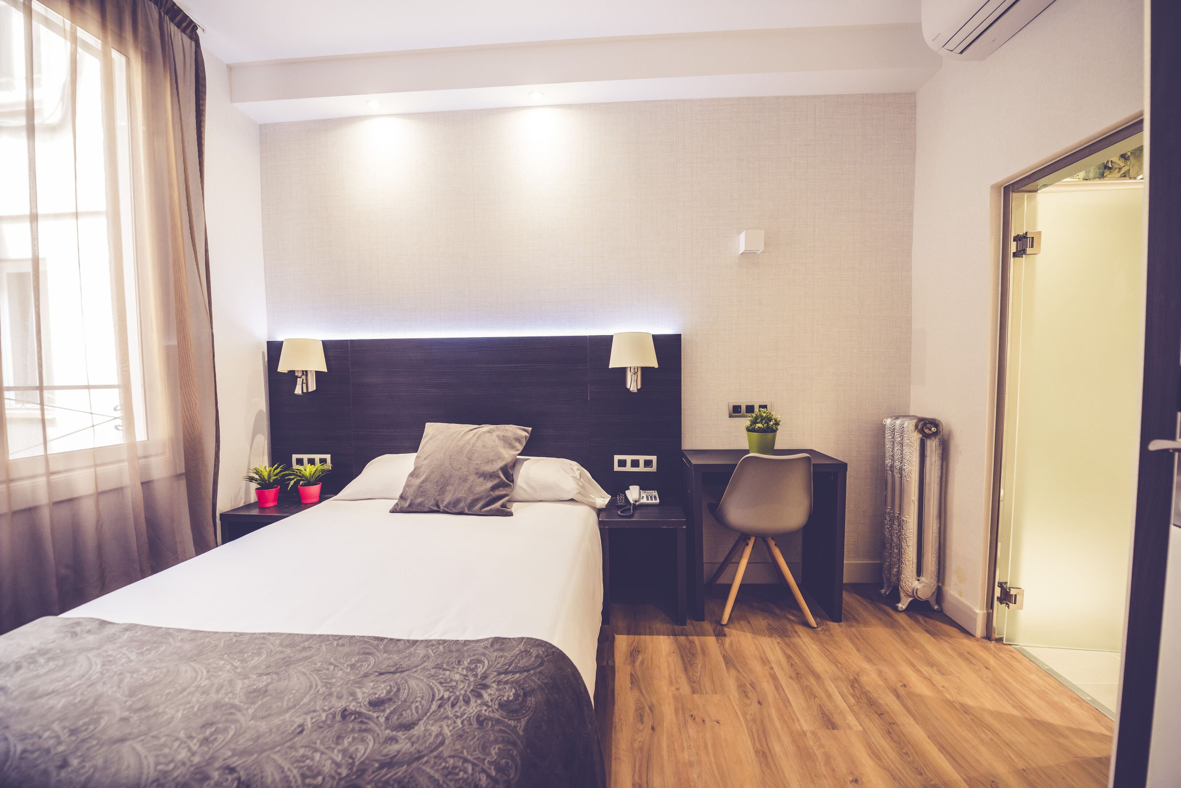 A hotel room with a large bed, bedside lamps, a desk with a chair, and a radiator.