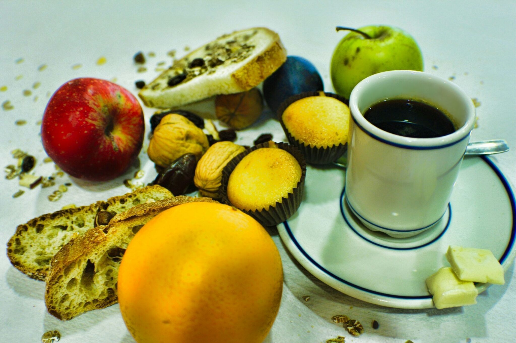 Une table mise pour le petit-déjeuner avec du pain, une pomme, un muffin, une tasse de café et une tranche de fromage sur une assiette.
