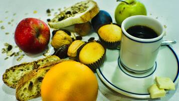 Une table mise pour le petit-déjeuner avec du pain, une pomme, un muffin, une tasse de café et une tranche de fromage sur une assiette.
