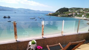 Un balcón con vista al mar tranquilo, una silla de madera y una mesita con flores.
