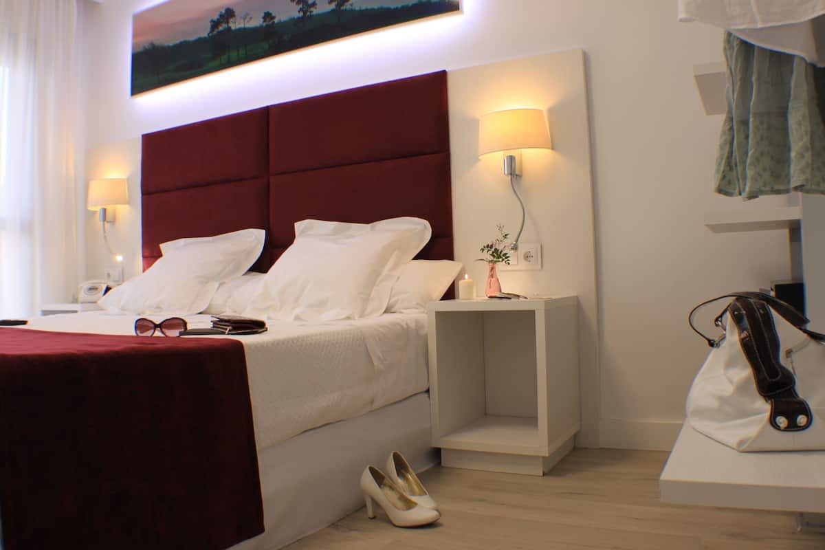 Habitación de hotel con cama, mesitas de noche, lámpara, bolso y un par de zapatos.