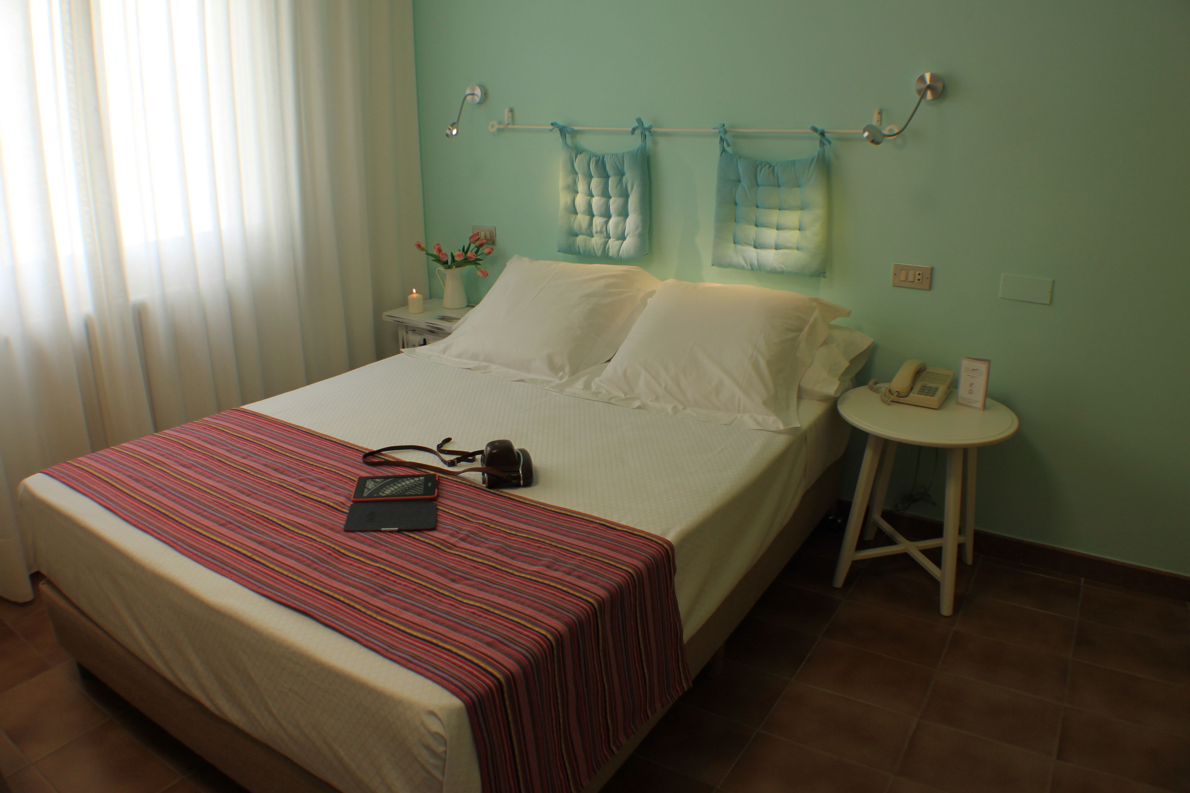 Una cama bien hecha con una colcha a rayas, una mesita de noche con una lámpara y un teléfono en la pared.