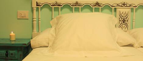 Una cama con ropa blanca, una mesita de noche color aguamarina con una vela y una cámara antigua sobre la cama.