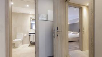 A hotel room with a wooden door, a bathroom with a toilet and sink, and a bed with pillows.