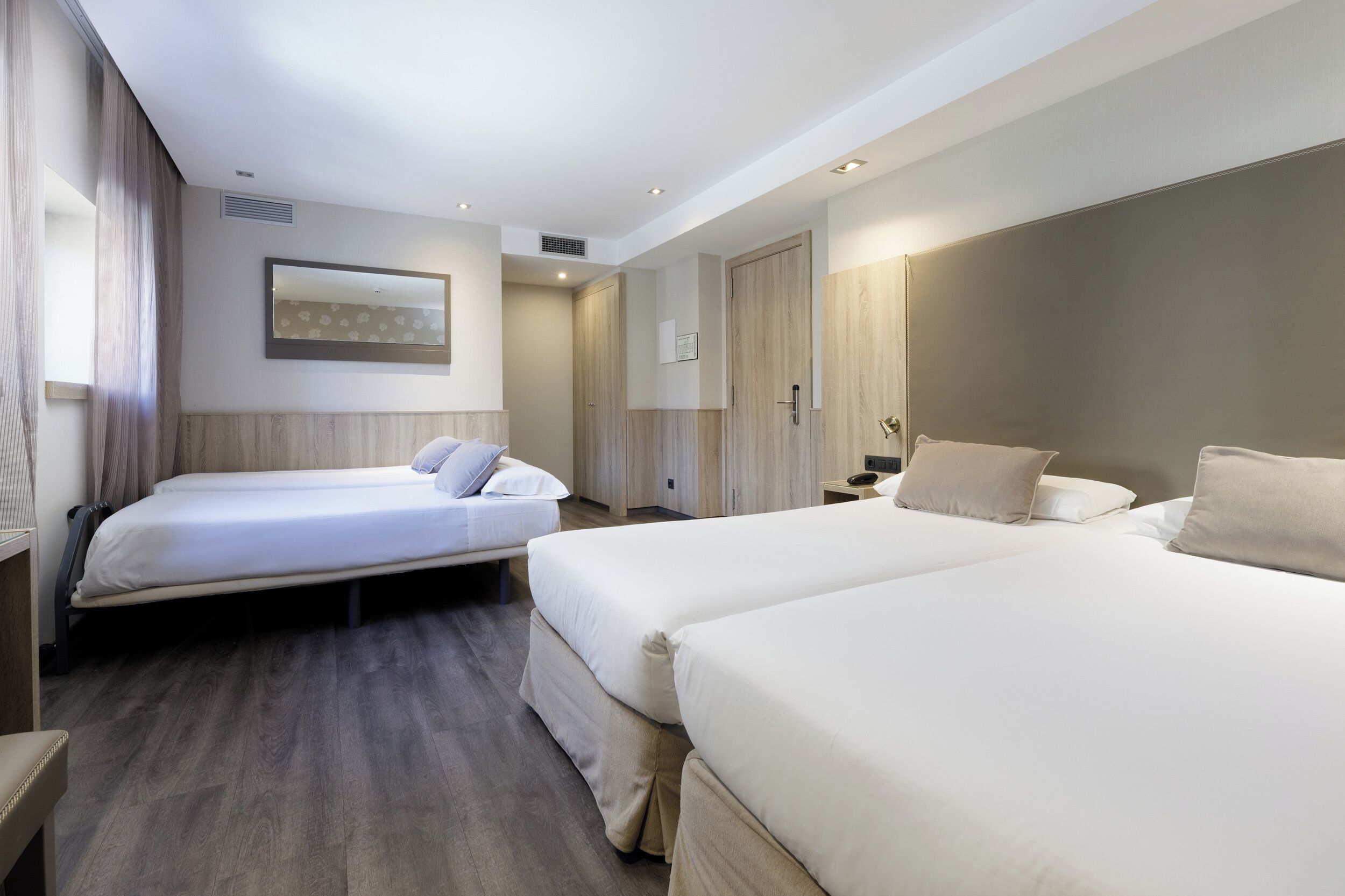 Habitació d'hotel amb dos llits, un mirall gran i un armari.