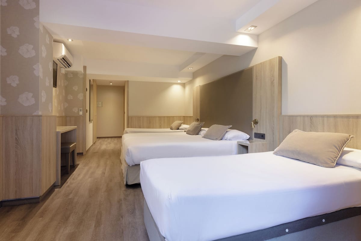 A hotel room with two beds, a wooden wardrobe, a desk, and a mirror.