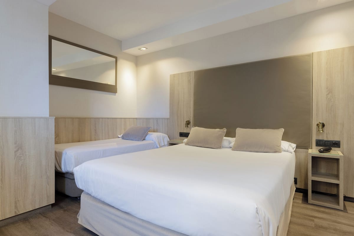 A modern hotel room with two beds, a large mirror, and a wooden wardrobe.