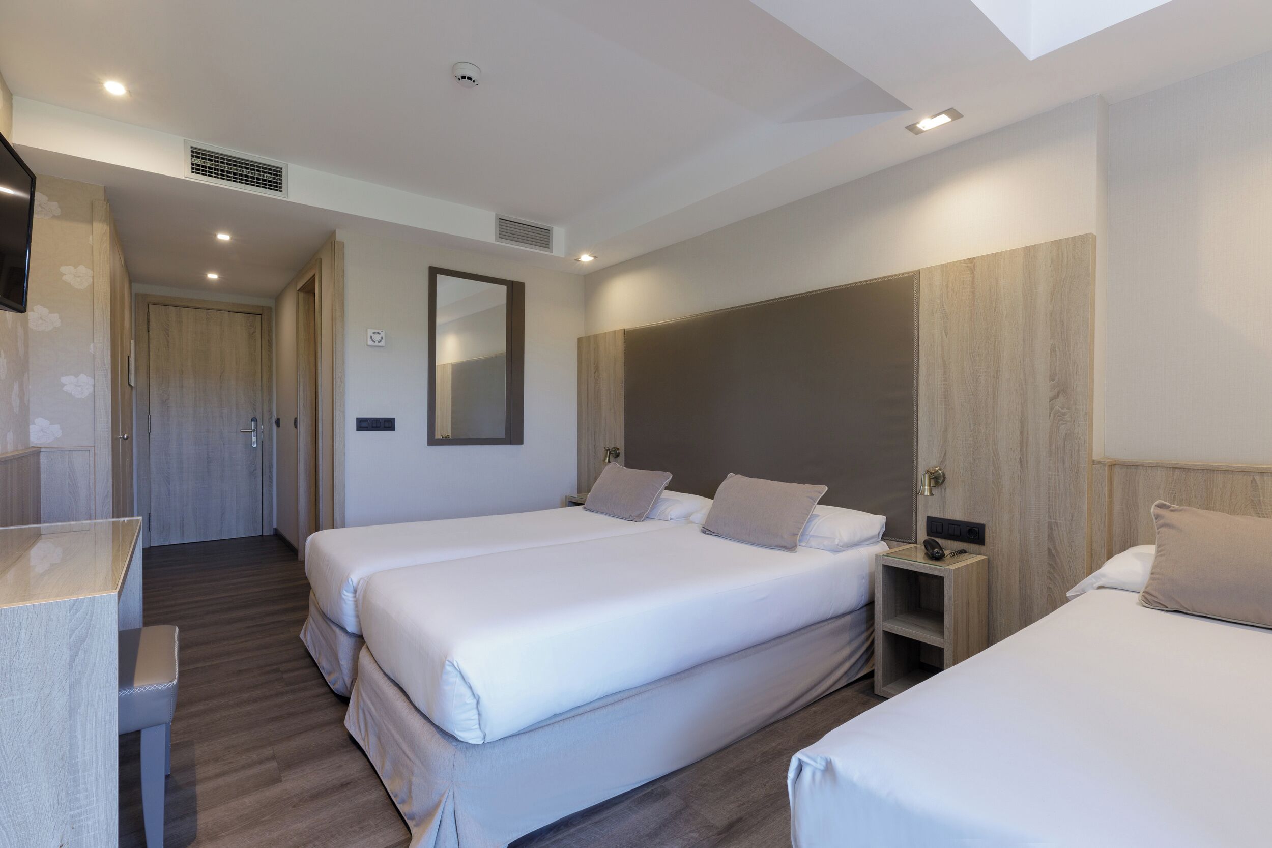 Habitación de hotel con dos camas, un escritorio y un espejo.