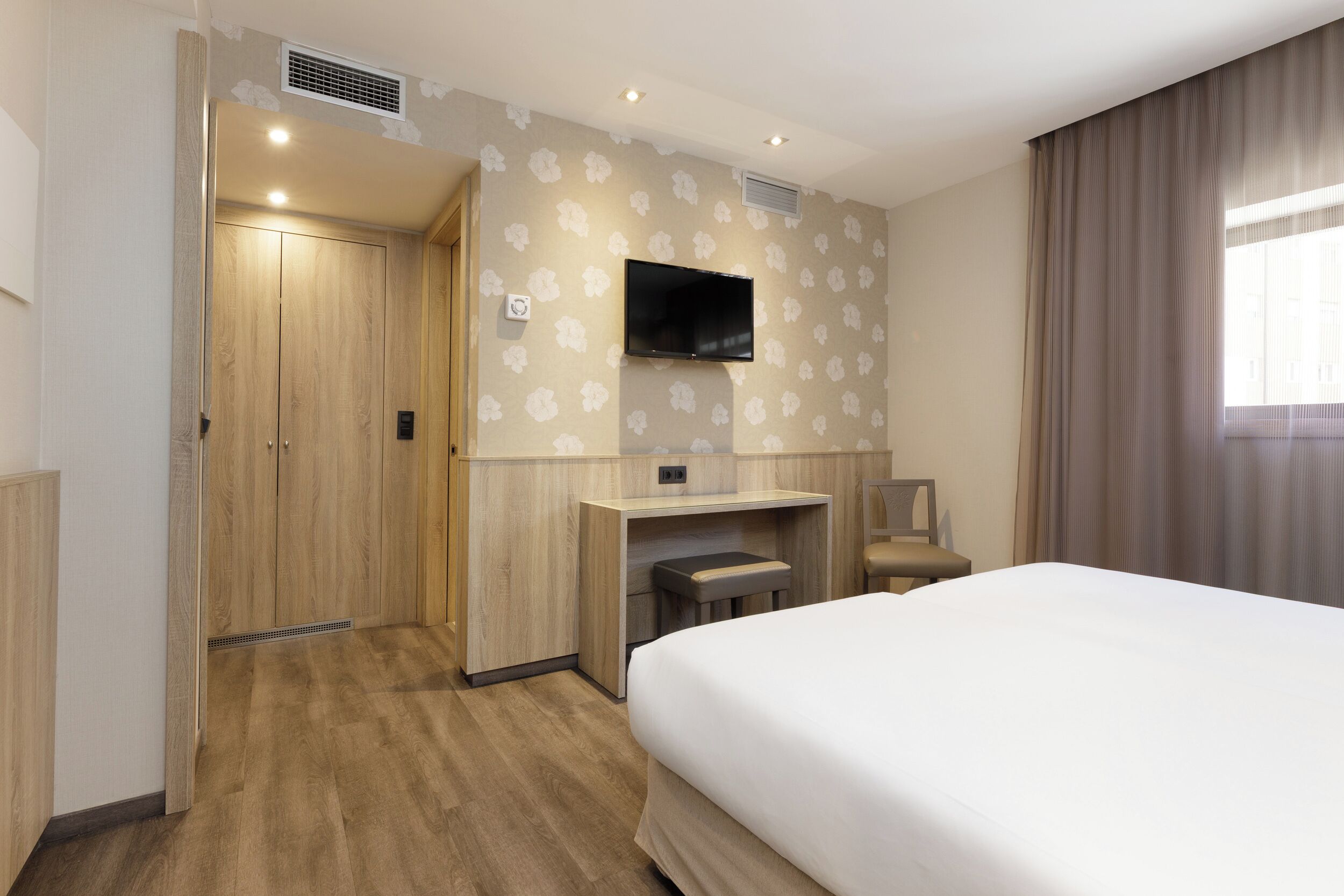 Una habitación de hotel con cama, escritorio, silla, televisor y armario.