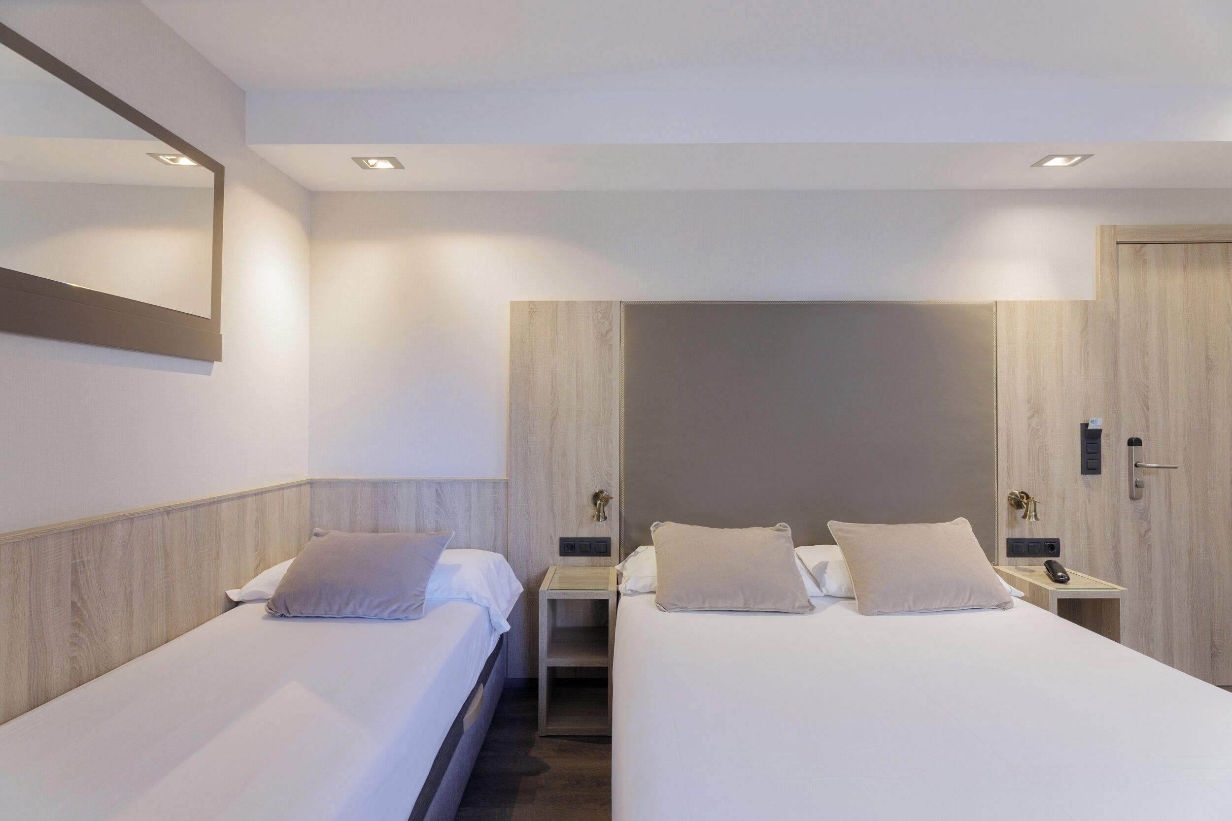 Habitación de hotel con dos camas, un espejo grande y un armario de madera.