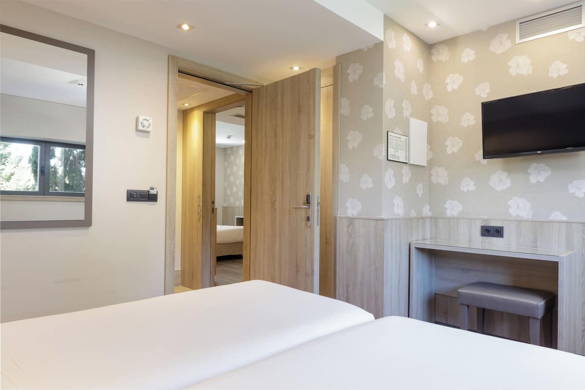 A modern hotel room with a large bed, a TV mounted on the wall, and a wooden wardrobe.