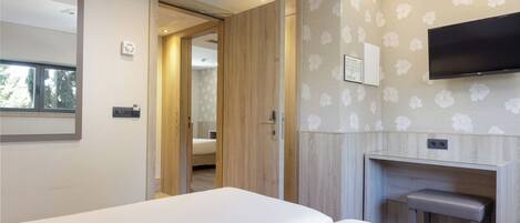 Una habitación de hotel moderna con una cama grande, un televisor montado en la pared y un armario de madera.