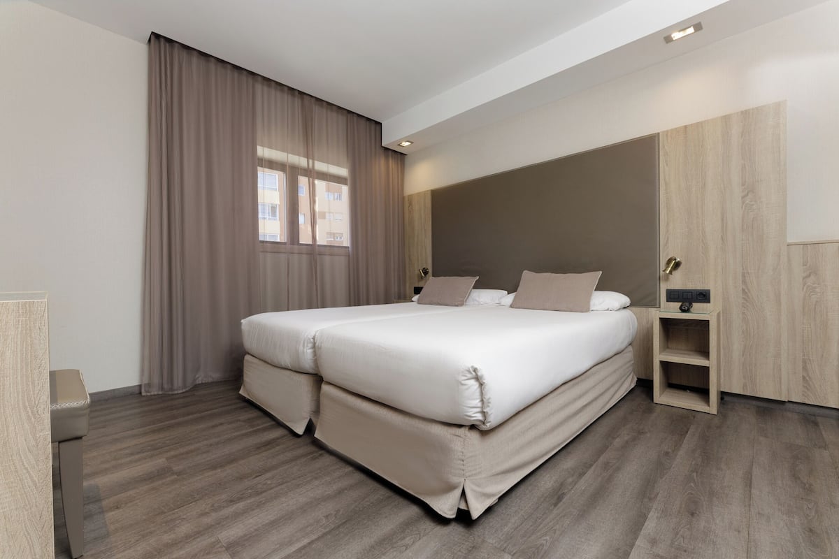 A modern hotel room with a large bed, a wooden wardrobe, and a small bedside table.