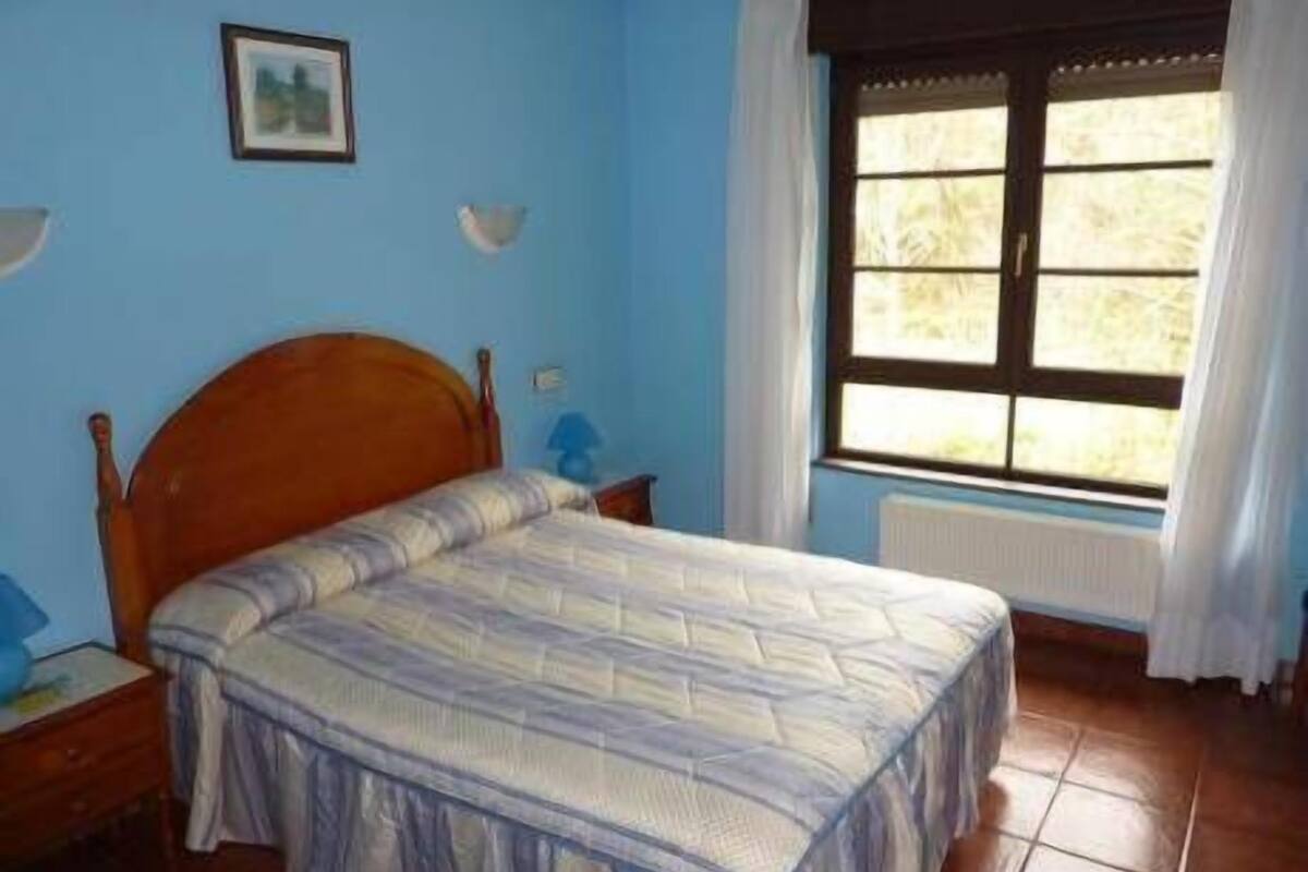 A bedroom with a wooden bed, a window with curtains, and a blue wall.