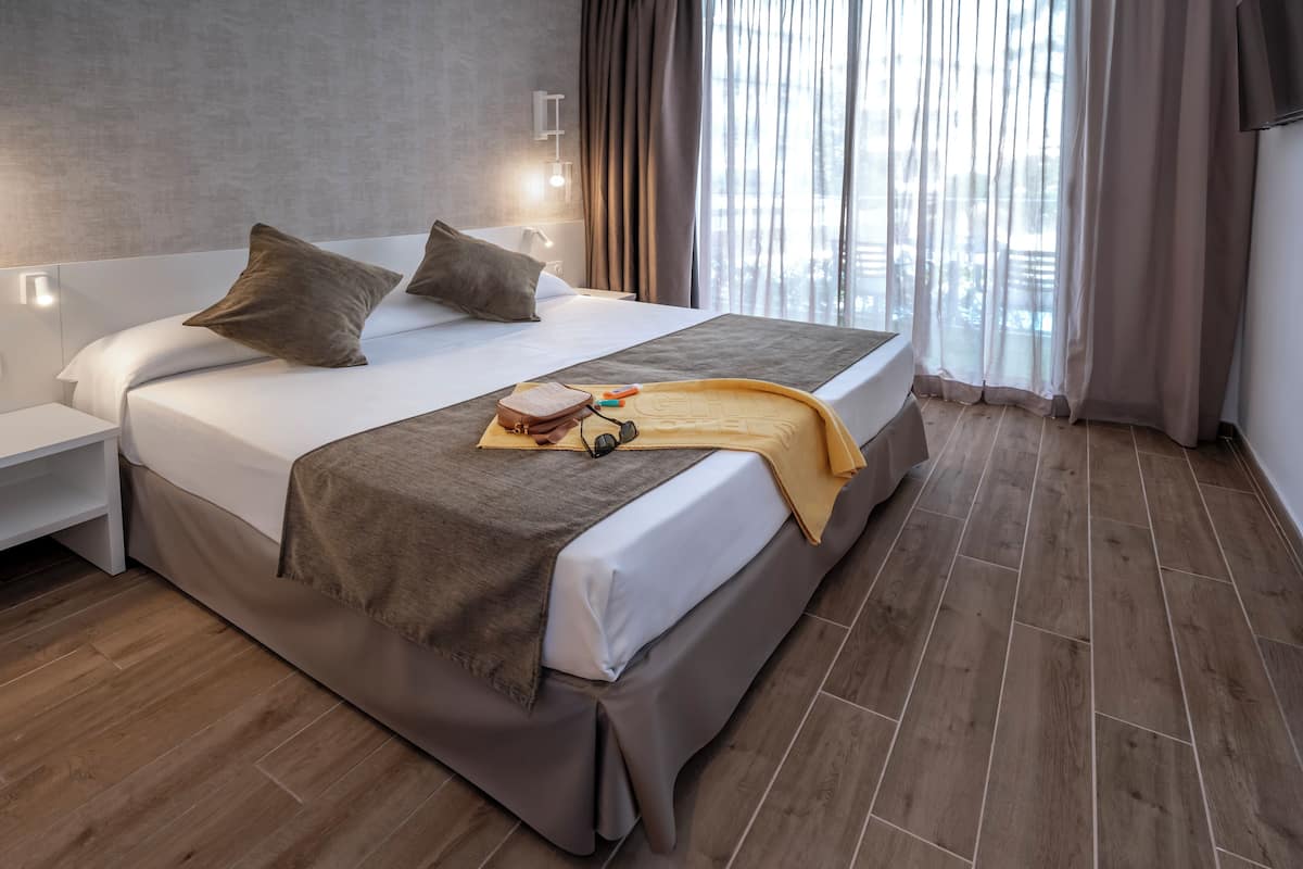 Een moderne hotelkamer met een groot bed, een nachtkastje en uitzicht op de stad door dunne gordijnen.