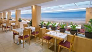 Un restaurant amb taules i cadires, plantes en testos i vistes a la platja.