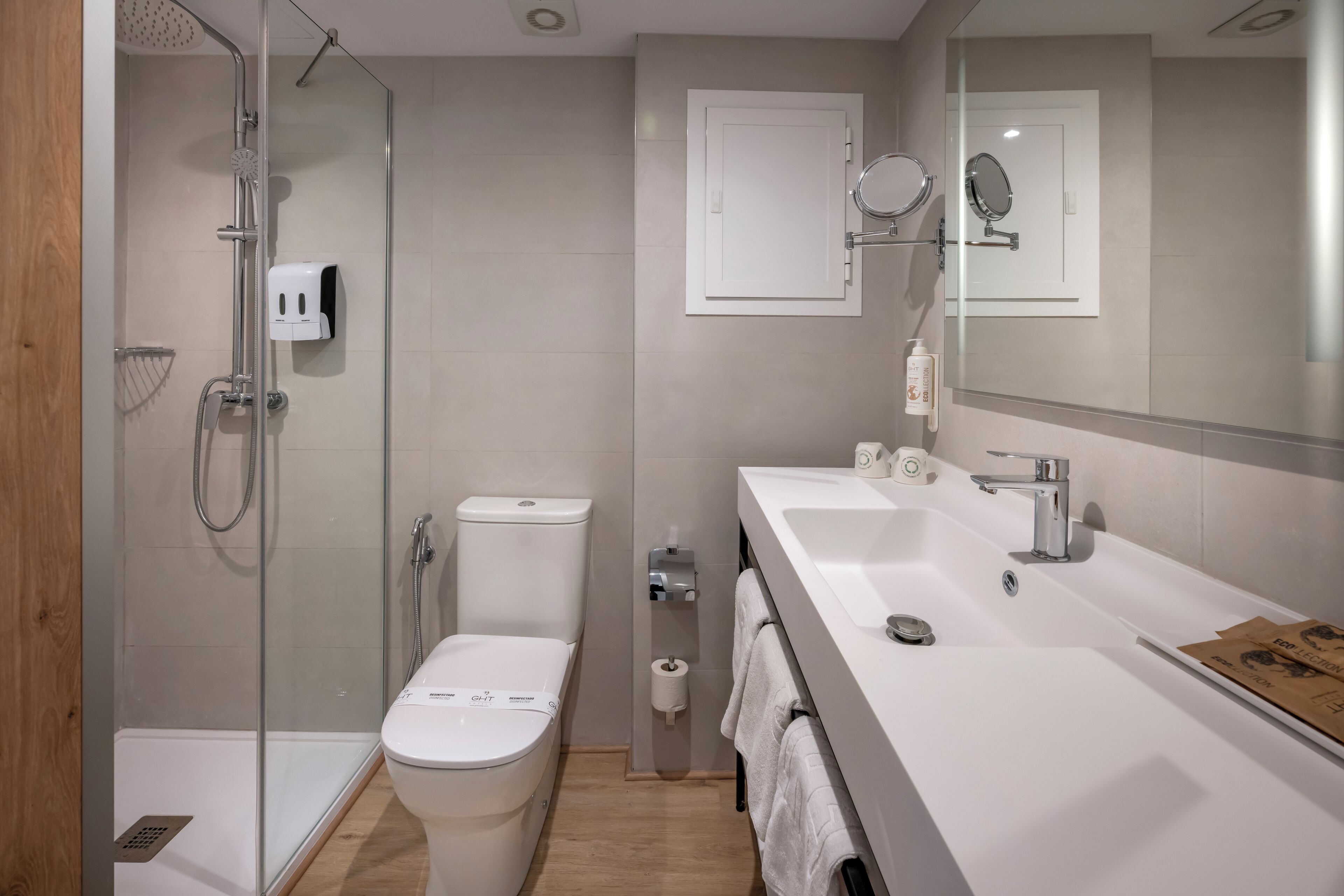 Un baño moderno con ducha de vidrio, inodoro, lavabo con espejo y un perchero para toallas.