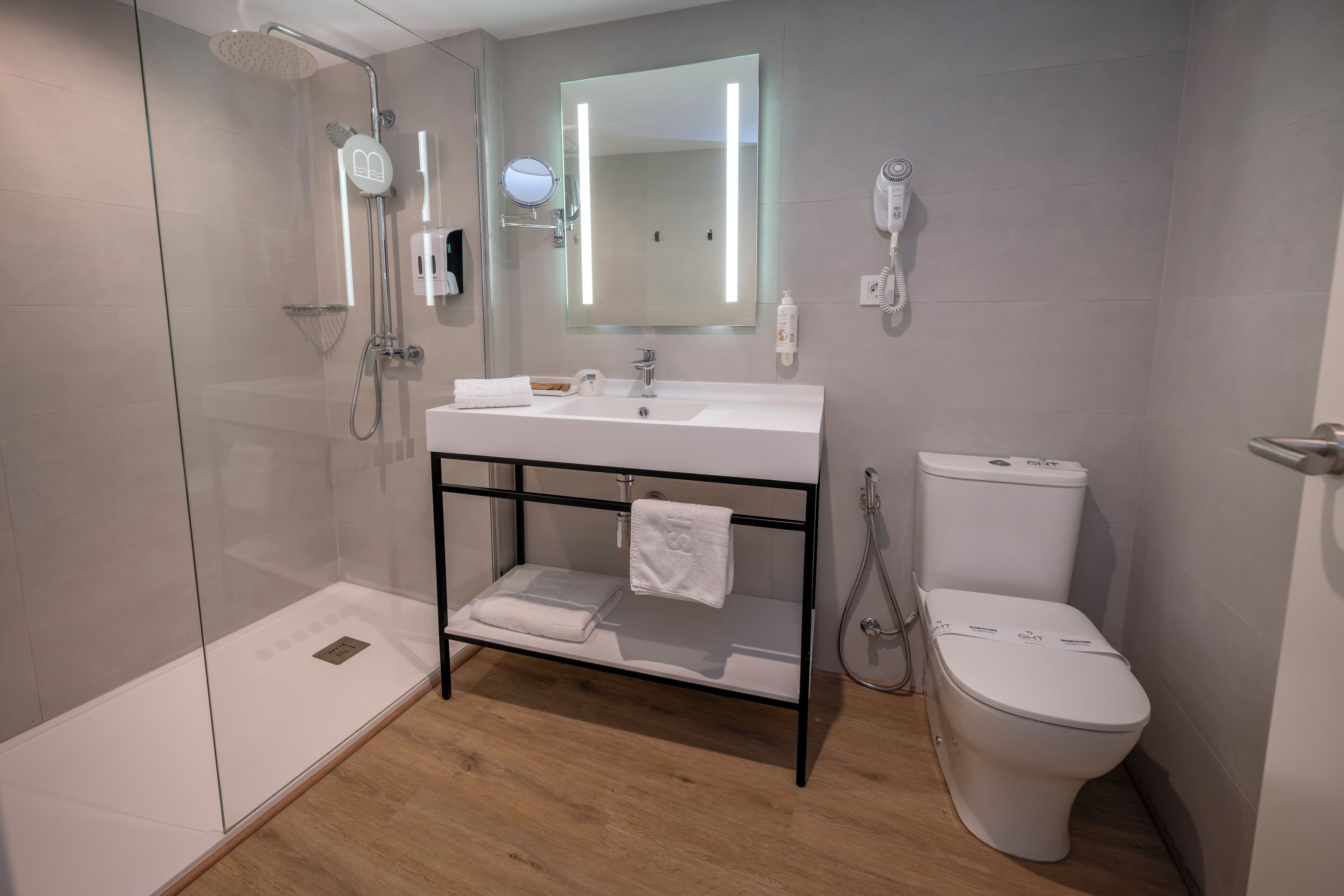 A modern bathroom with a glass-enclosed shower, a white sink with a black frame, a large mirror, and a white toilet.