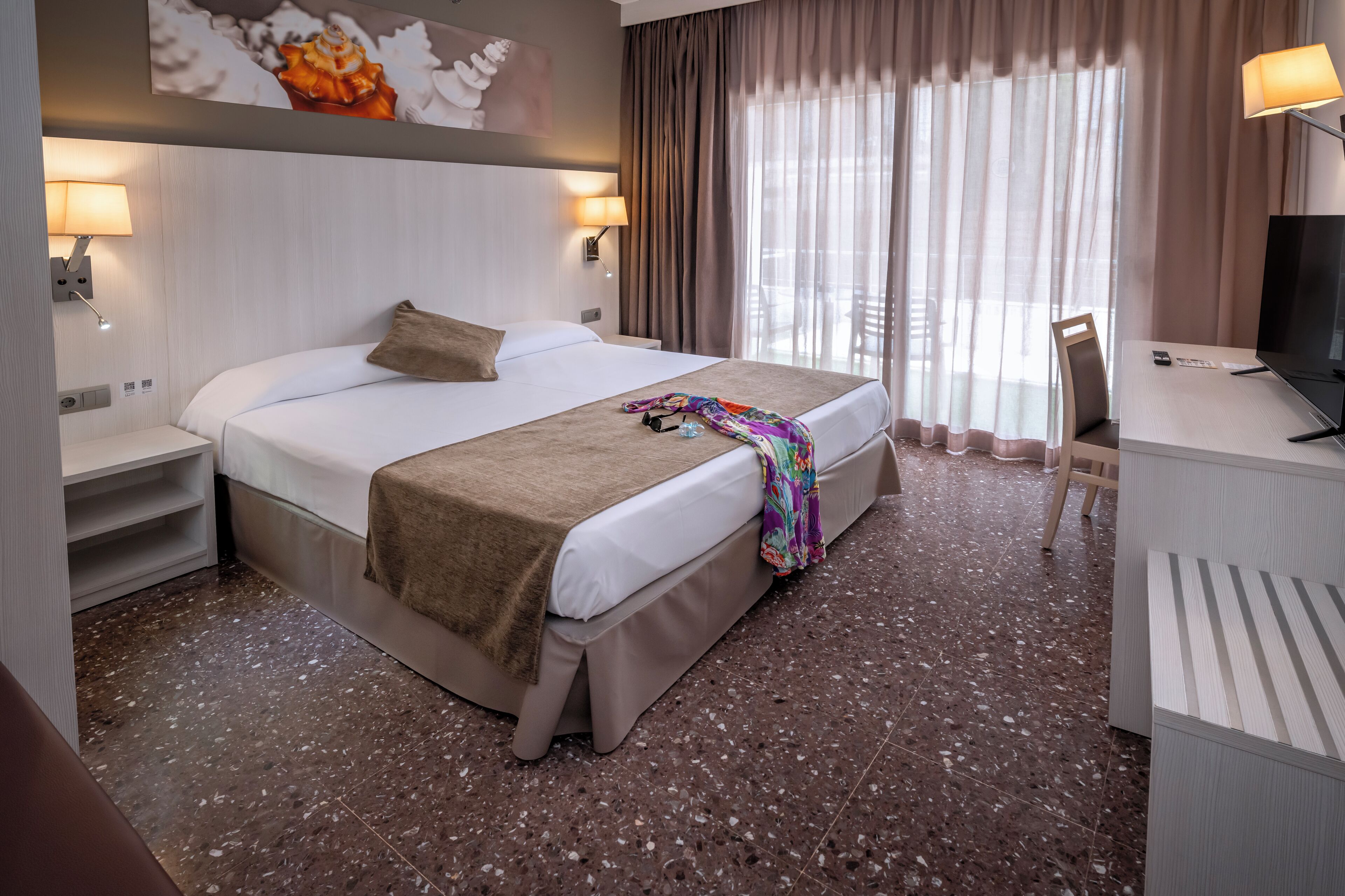 Una habitación de hotel con una cama grande, un escritorio con televisor y una silla.