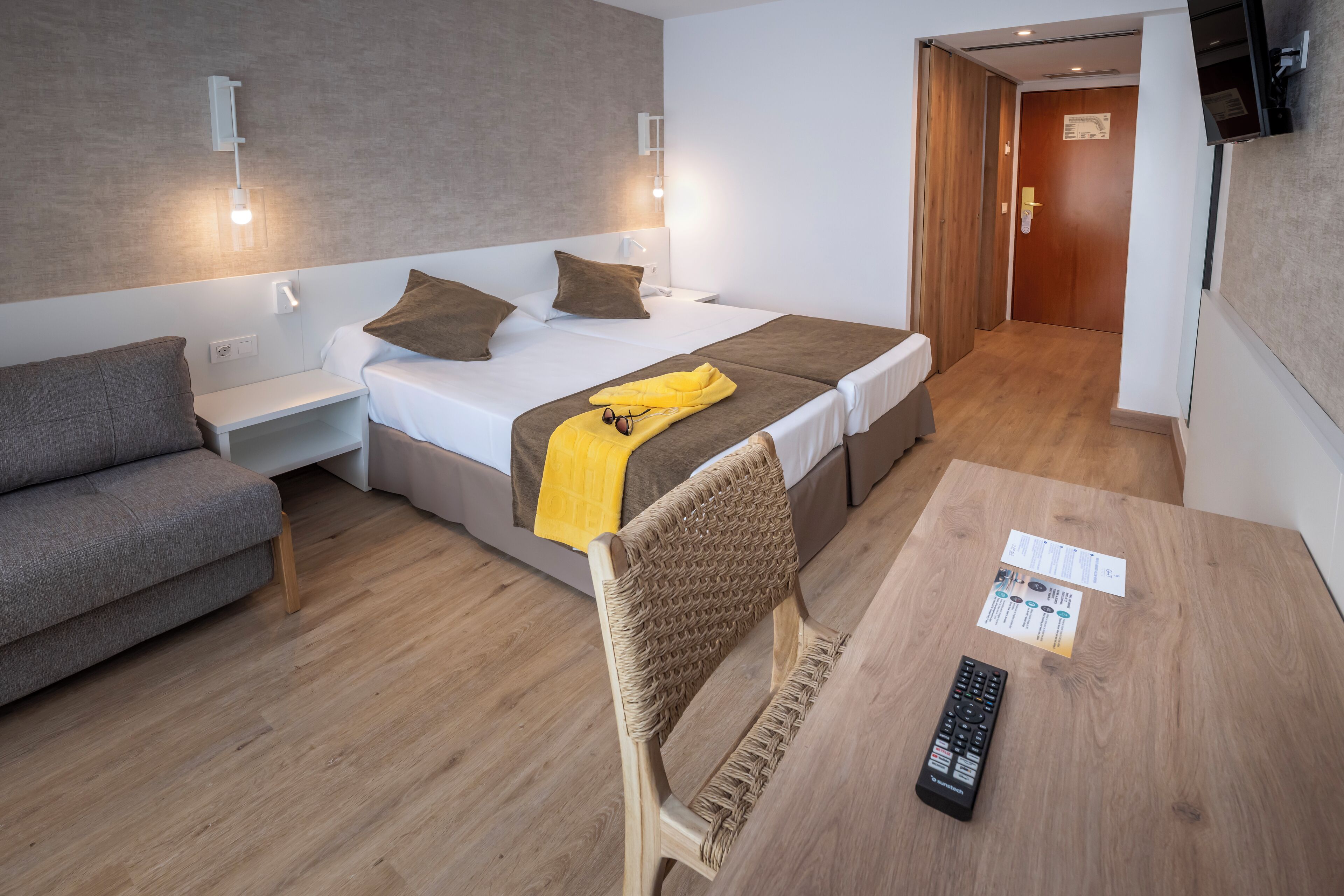 Una habitación de hotel con una cama, un sofá, una mesa con un control remoto y una silla.