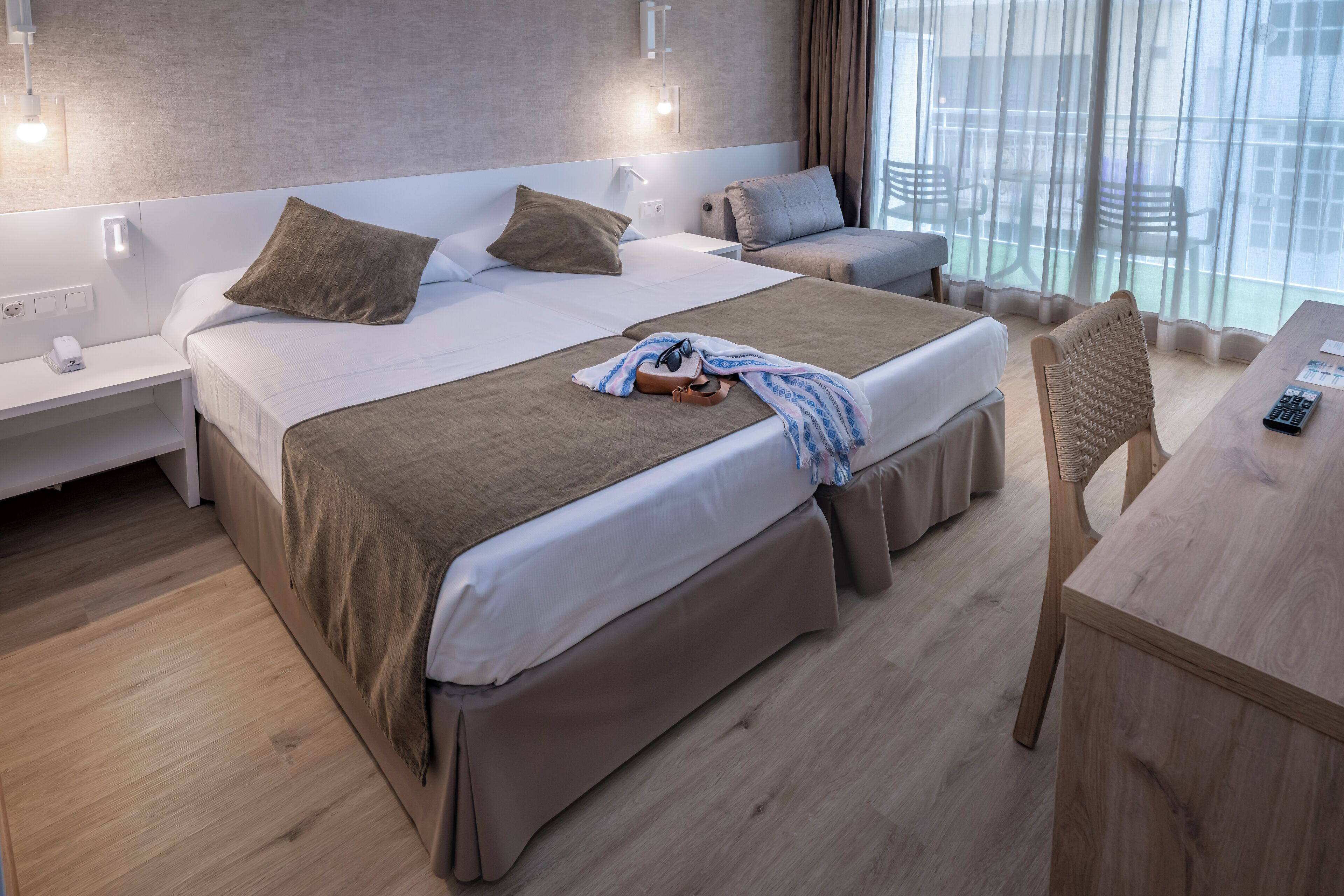 Habitación de hotel moderna con una cama grande, un escritorio de madera y vistas al exterior a través de cortinas translúcidas.