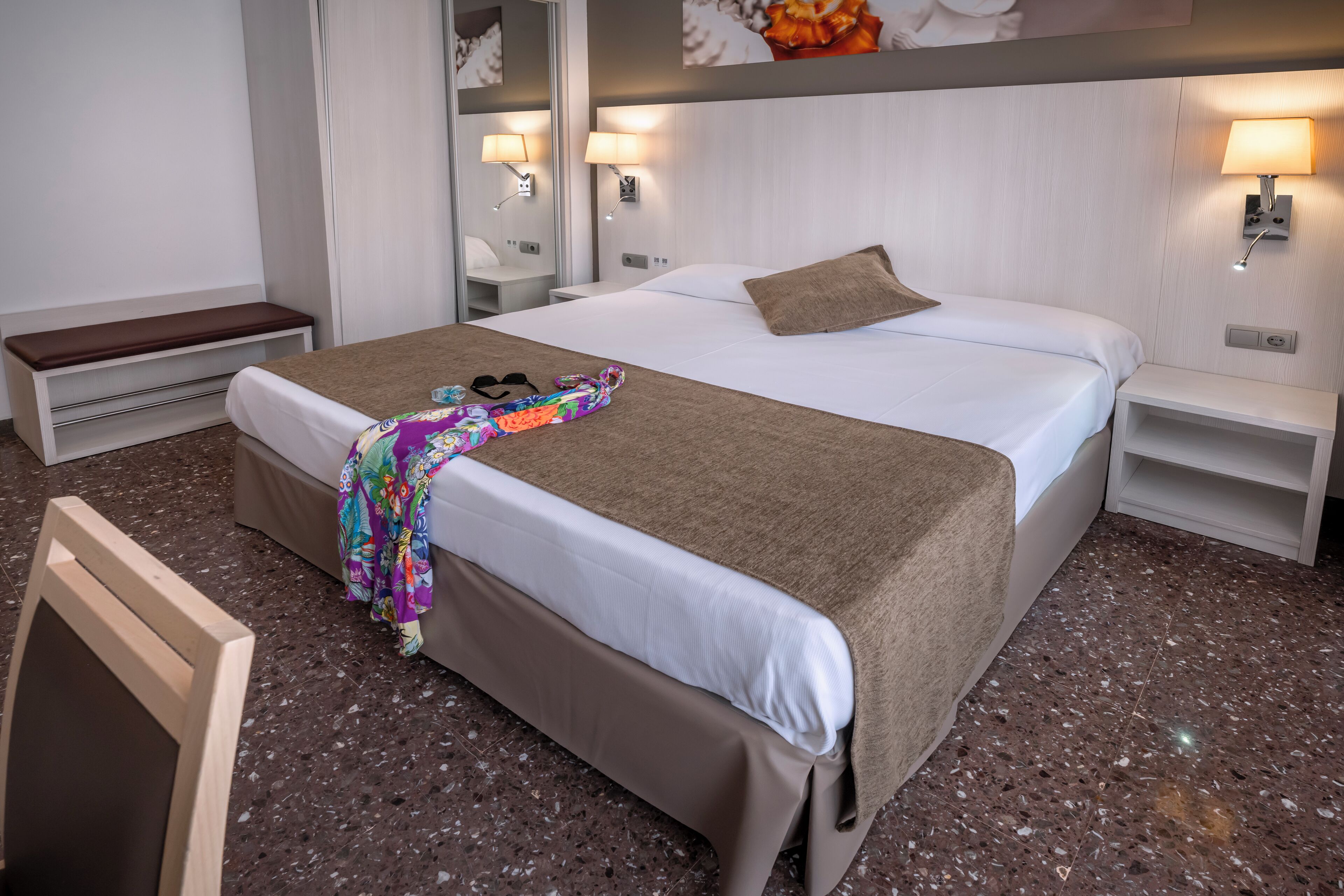 Una habitación de hotel con una cama grande, un banco, una mesita de noche y un espejo.