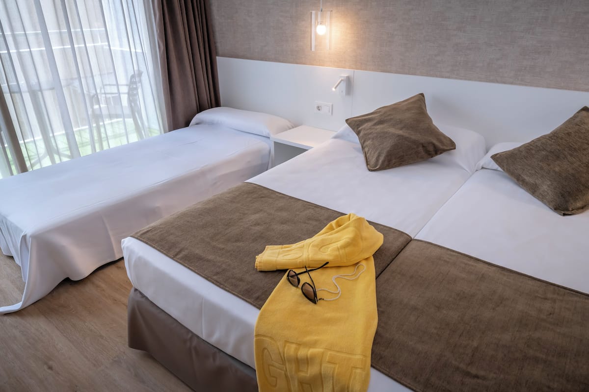 Een hotelkamer met twee eenpersoonsbedden, een groot bed en een nachtkastje met een lamp.