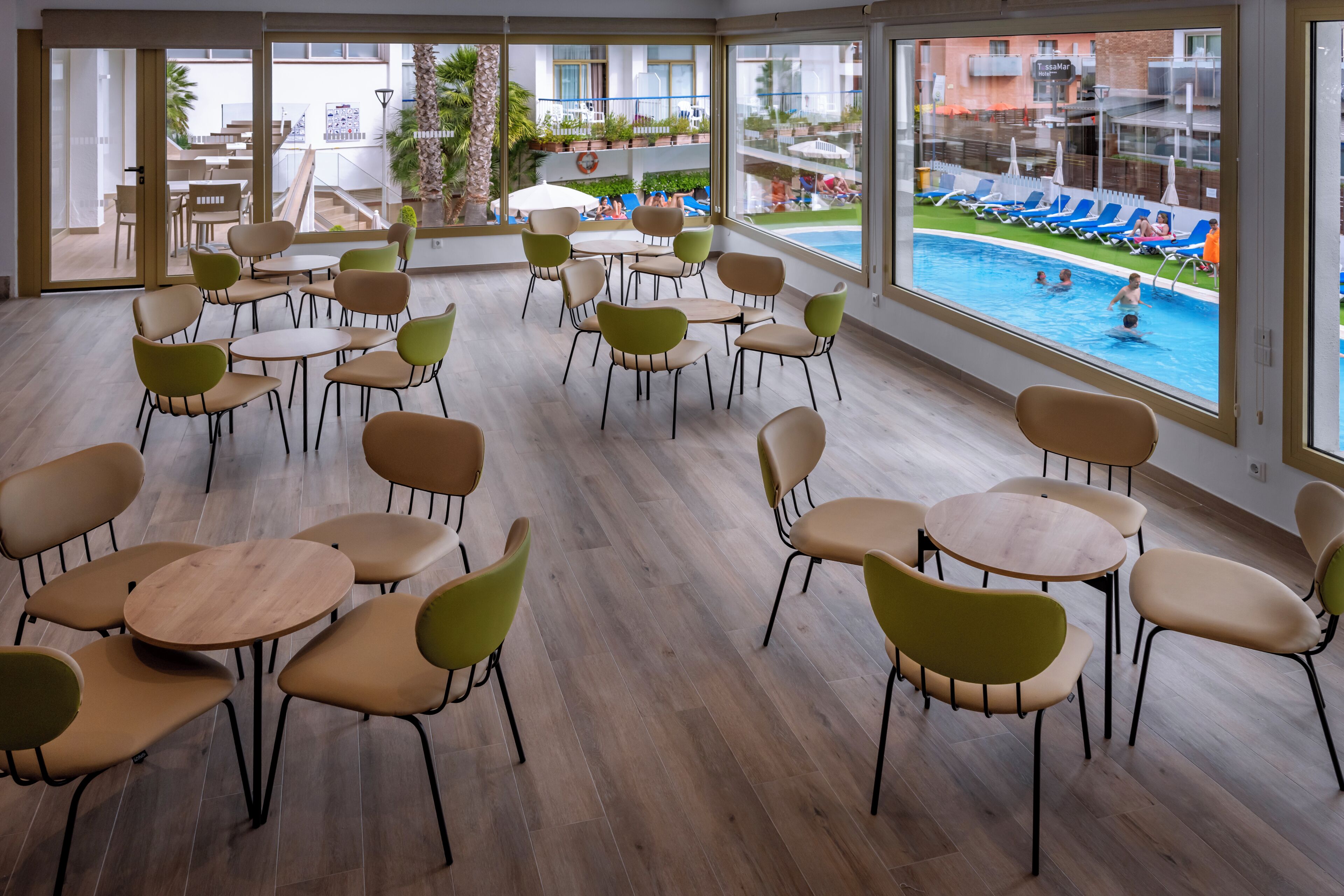 Habitación de hotel con vista a una piscina, varias zonas de estar y una escalera que conduce a una terraza exterior.