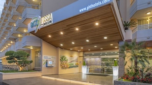 A hotel entrance with a modern design, a website address, and an auto check-in kiosk. - Hotel GHT Oasis Tossa & Spa (Tossa de Mar)