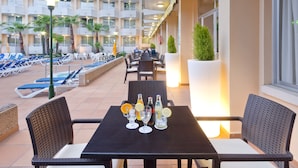 A hotel lounge with outdoor seating, a pool, and a view of the building's balconies. - Hotel GHT Oasis Tossa & Spa (Tossa de Mar)