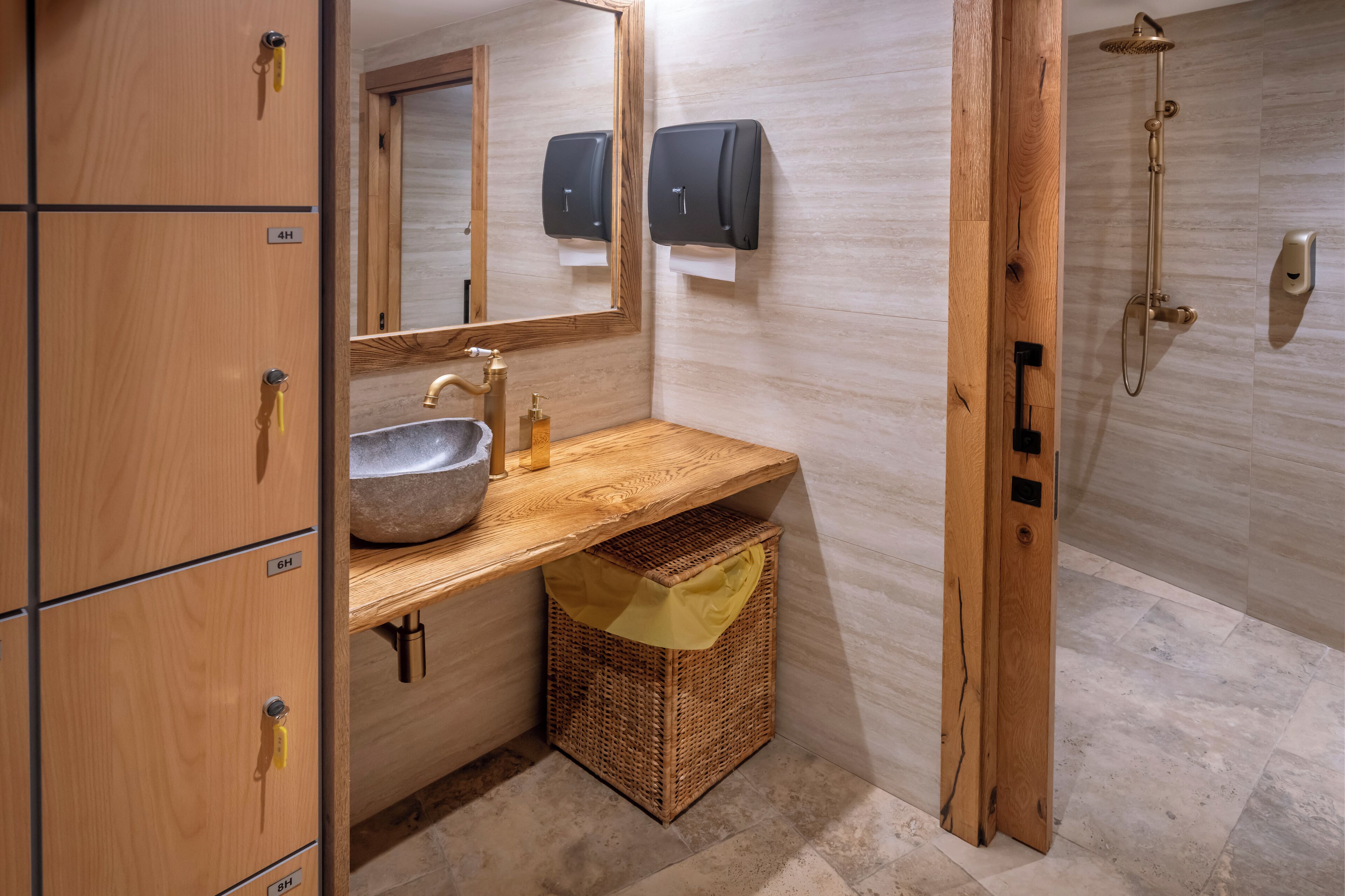 Une salle de bain avec des meubles en bois, un lavabo, un miroir, une douche et un distributeur de serviettes.